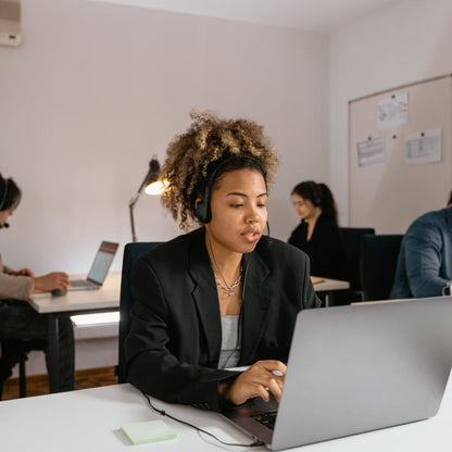 Mujer joven con auriculares trabajando con compra de reseñas y reputación online en un ordenador portátil en una moderna oficina central de Rating Leader reputación online